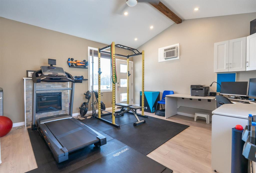 Family room/gym/home office has vaulted ceiling with electric fireplace